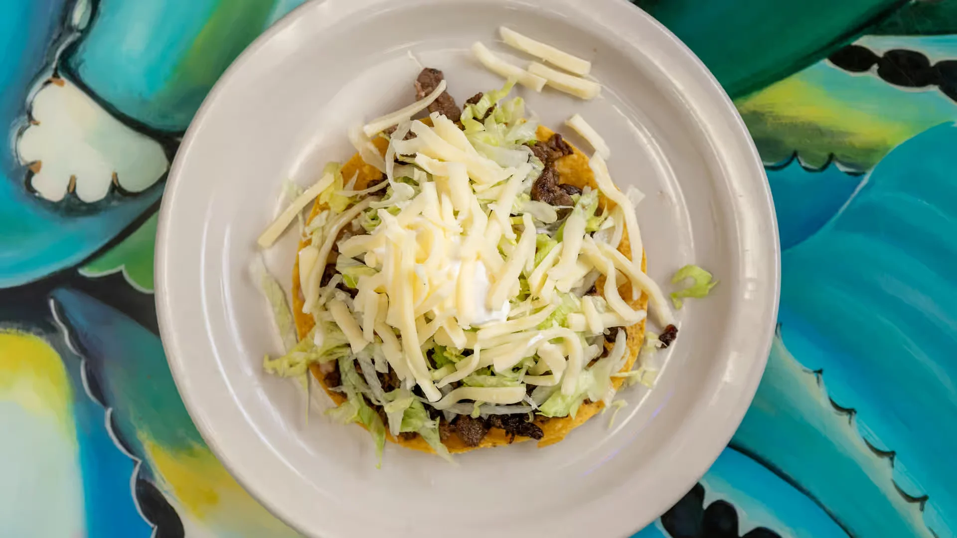Tostada - Crispy fried tortilla topped with beans, meat, lettuce, and cheese
